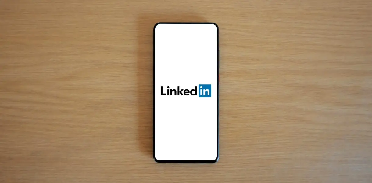 Top view of a smartphone displaying the LinkedIn logo on a wooden surface.
