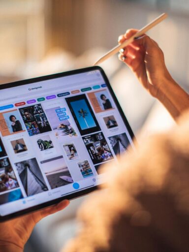 A person uses a digital tablet with a stylus indoors in a warm, cozy setting.
