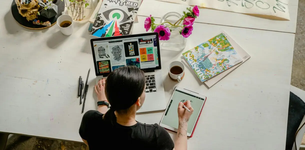 Artistic workspace featuring calligraphy and digital design on a tablet and laptop.