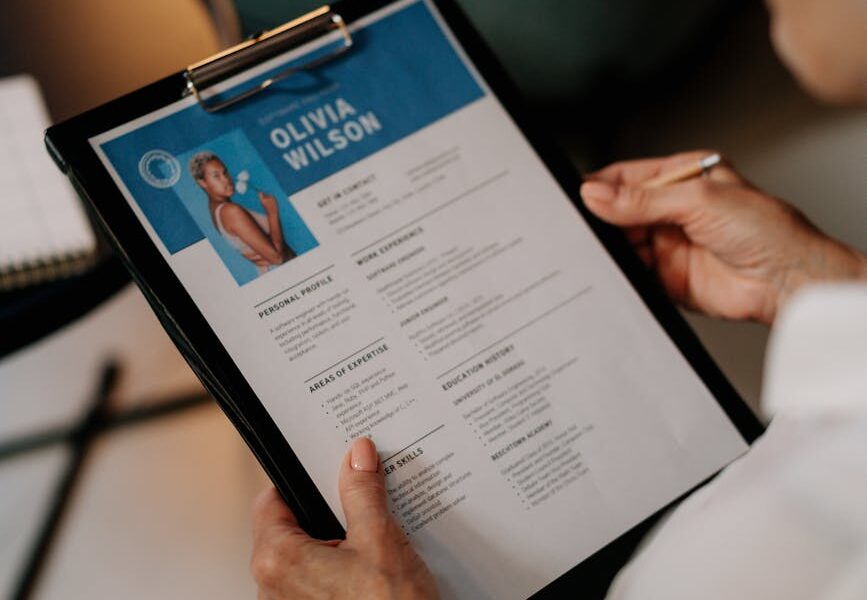 An HR professional reviews a resume on a clipboard during an office meeting.