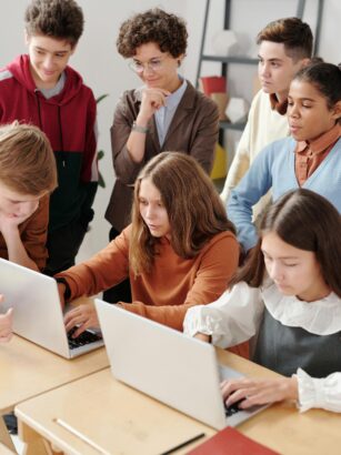 Group of teenagers in a classroom collaboratively working on laptops, fostering team learning.